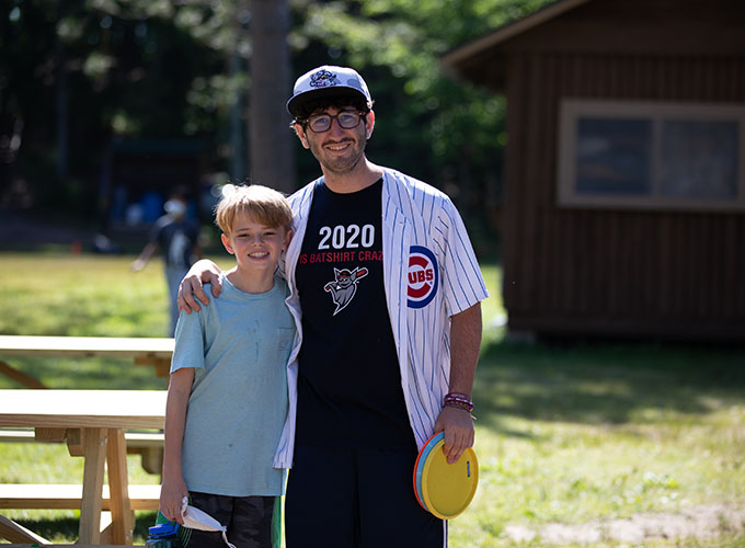 A camper and staff member smile with their arms around each other carrying frisbee discs at North Star Camp for Boys.
