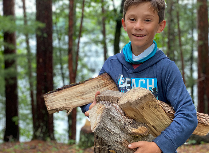A young camper smiles while carrying an armful of firewood during a wilderness skills exercise at North Star Camp for Boys.