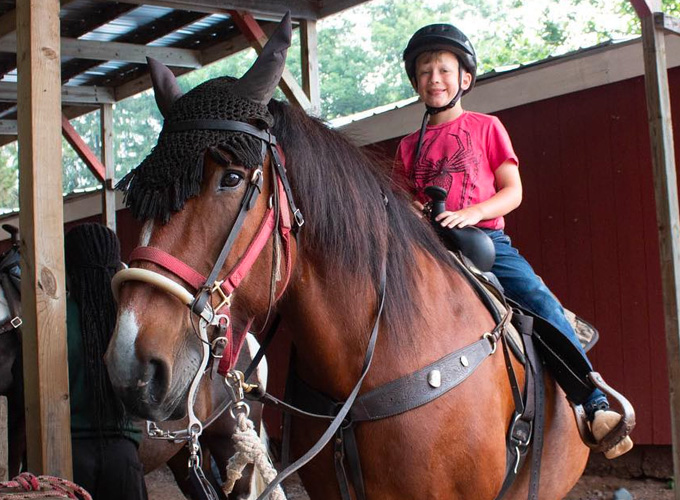 A camper from North Star Camp for Boys smiles while on horseback.