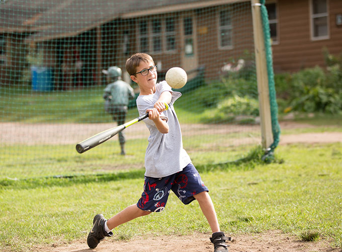 A camper swings a softball bat at an incoming ball during a game at North Star Camp for Boys.