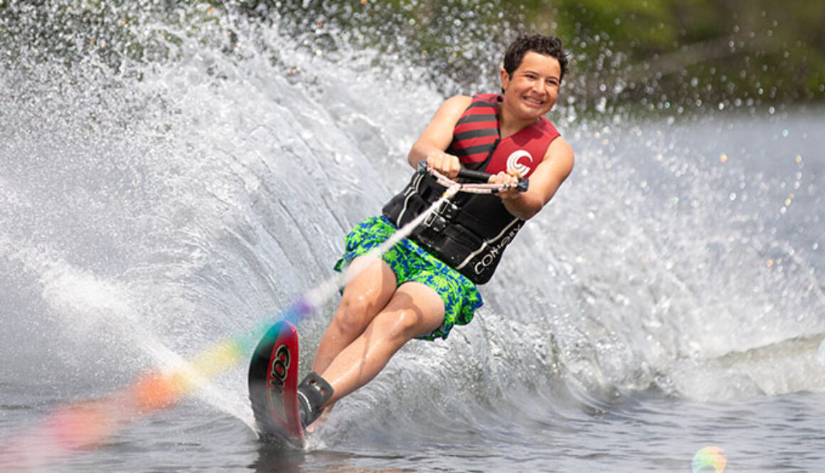 A camper smiles as he slalom waterskies through spider lake, leaving a fountain of water in his trail at North Star Camp for Boys.