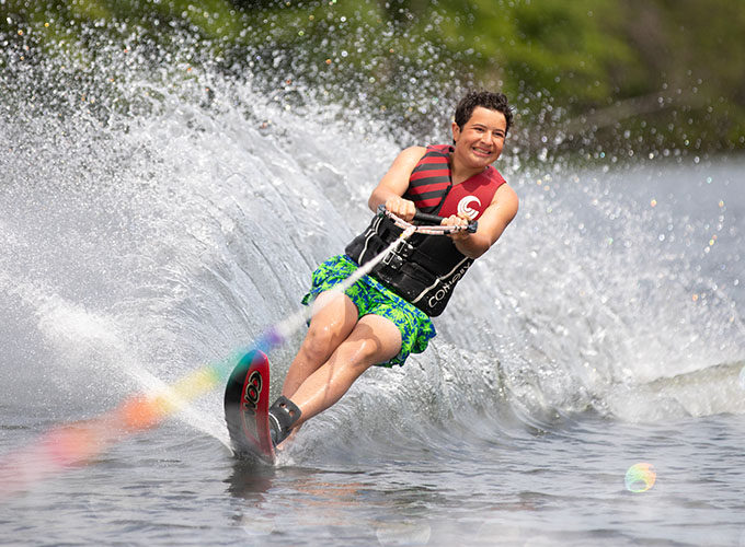 A camper smiles as he slalom waterskies through spider lake, leaving a fountain of water in his trail at North Star Camp for Boys.