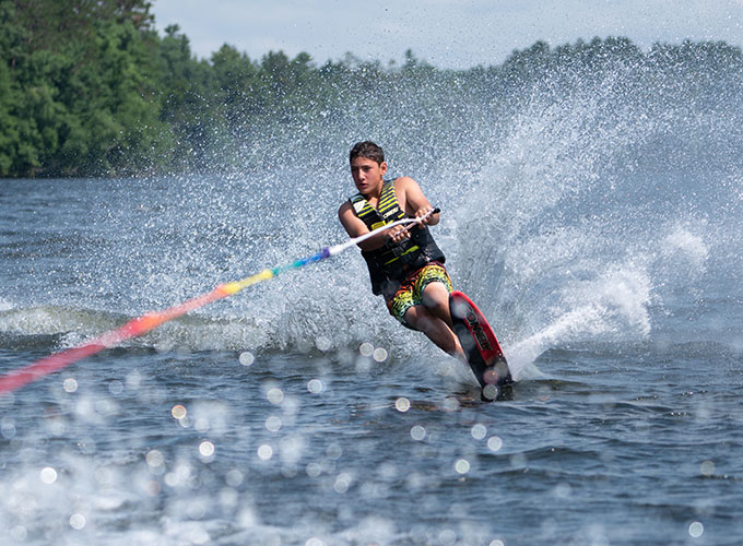 A camper slalom waterskies through Spider Lake, leaving a gust of waves behind him at North Star Camp for Boys.