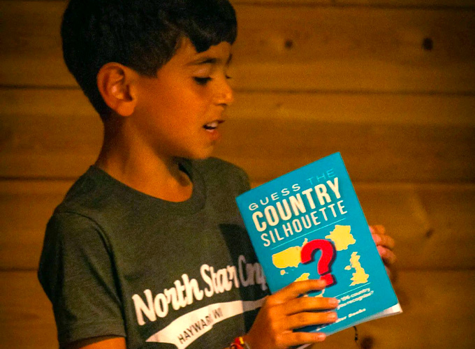 A camper at North Star Camp for Boys performs during a theater improv activity holding a pamphlet entitled "Guess the Country Silhouette".