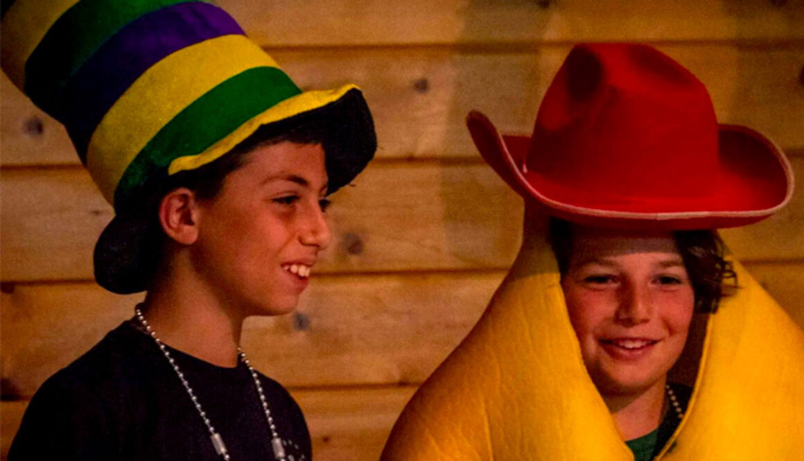 Two campers at North Star Camp for Boys dressed in large hats and costumes participate in a theater improv activity.