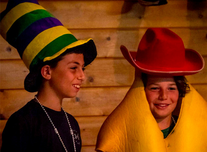 Two campers at North Star Camp for Boys dressed in large hats and costumes participate in a theater improv activity.