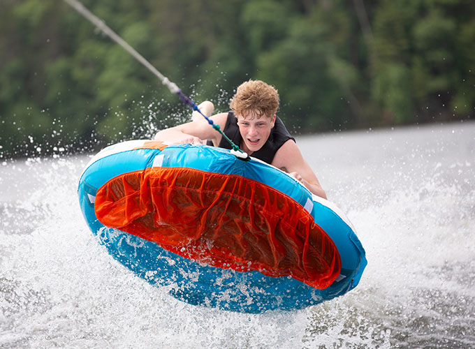 A camper jumps out of the water while gripping a tube in Spider Lake at North Star Camp for Boys.