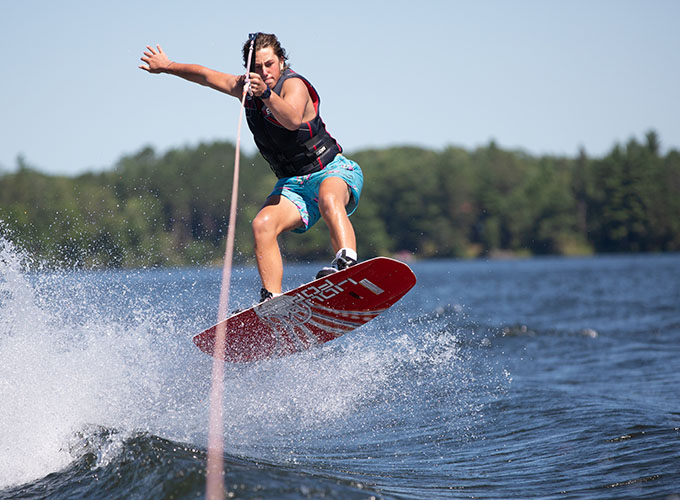 A camper performs a jumping trick in the air while on a wakeboard in Spider Lake at North Star Camp for Boys.