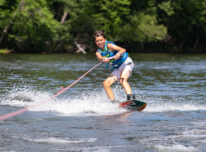 A camper stands on a wakeboard as he glides through Spider Lake at North Star Camp for Boys.