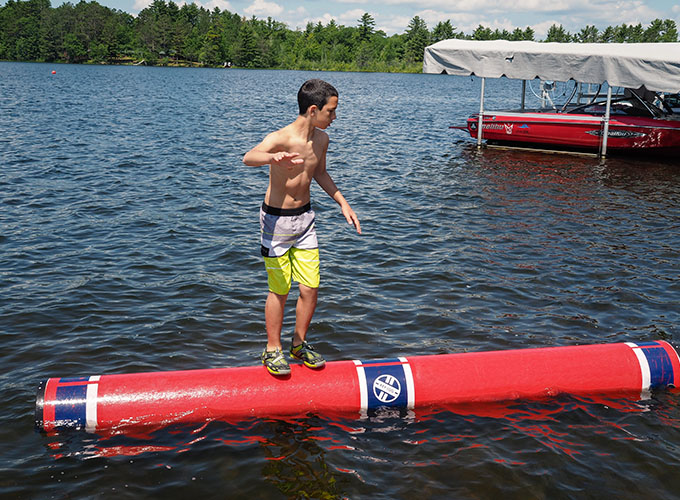 A boy balances on a water log roller on Spider Lake at North Star Camp for Boys.