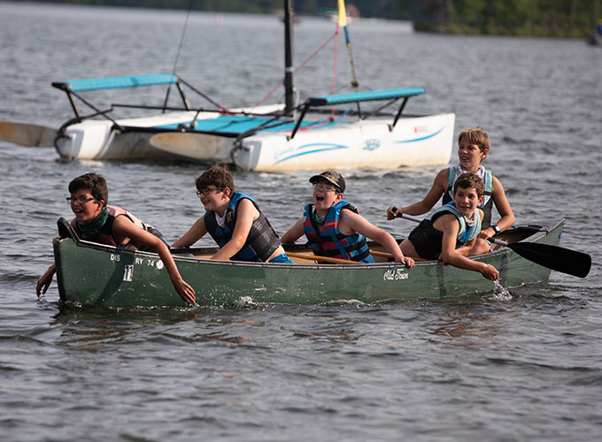 Five North Star Camp for Boys campers all look in the same direction while in a canoe on Spider Lake. The camper in the back holds an ore, while the four other campers have their hands in the water.