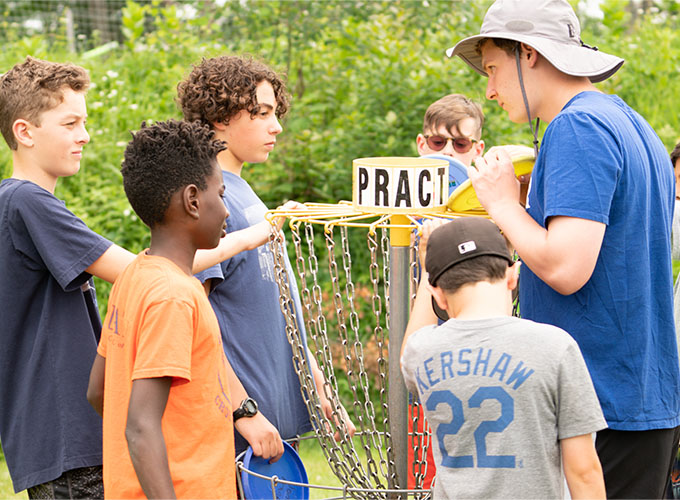Campers have serious looks on their faces as they huddle around a disc golf basket at North Star Camp for Boys.