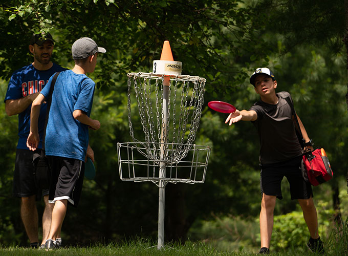 A camper throws a red frisbee to the disc golf basket at North Star Camp for Boys.