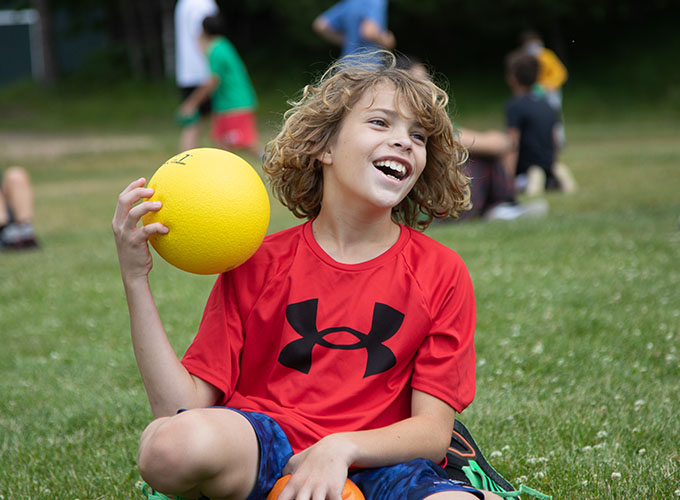 A camper smiles while holding a yellow foam ball used for dodgeball at North Star Camp for Boys.