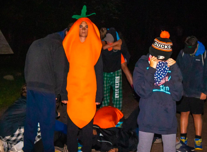 A camper wearing a carrot costume poses for a photo while other campers look down during a game of Espionage at North Star Camp for Boys.