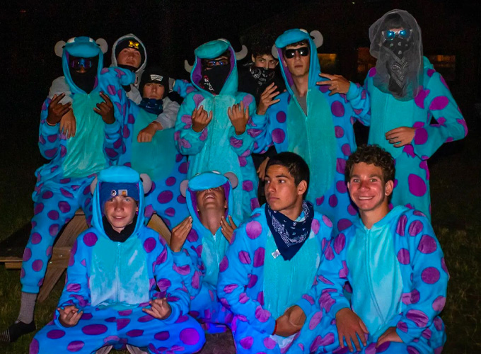 A group of campers wearing matching blue and purple onesies pose for a photo during a game of Espionage at North Star Camp for Boys.