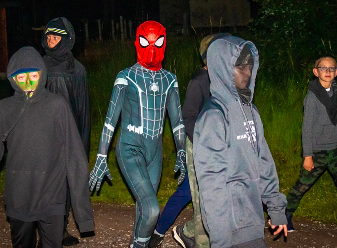 A group of campers dressed in all black costumes, face paint, and one in a Spiderman costume walk around while participating in a game of Espionage at North Star Camp for Boys.