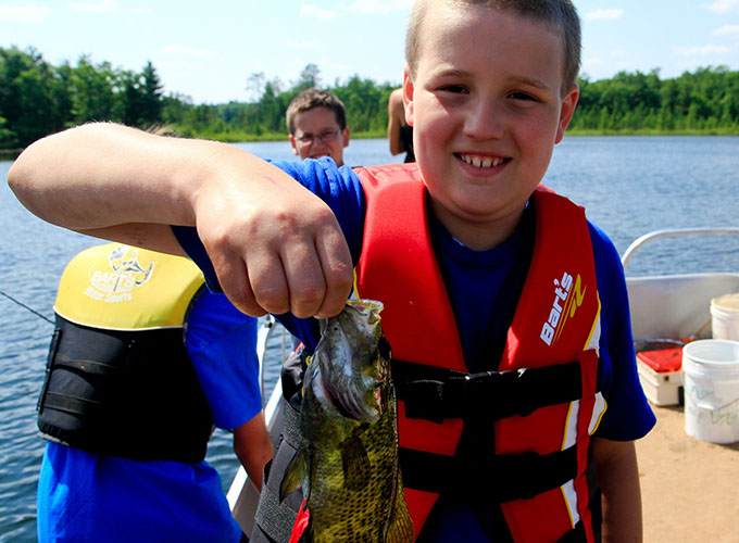 A camper smiles while holding up a fish he caught out of Spider Lake at North Star Camp for Boys.