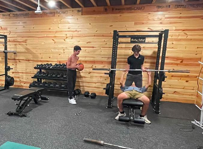 Campers use the weightlifting equipment at the gym at North Star Camp for Boys. Two boys are spotting the one boy lifting the bar.