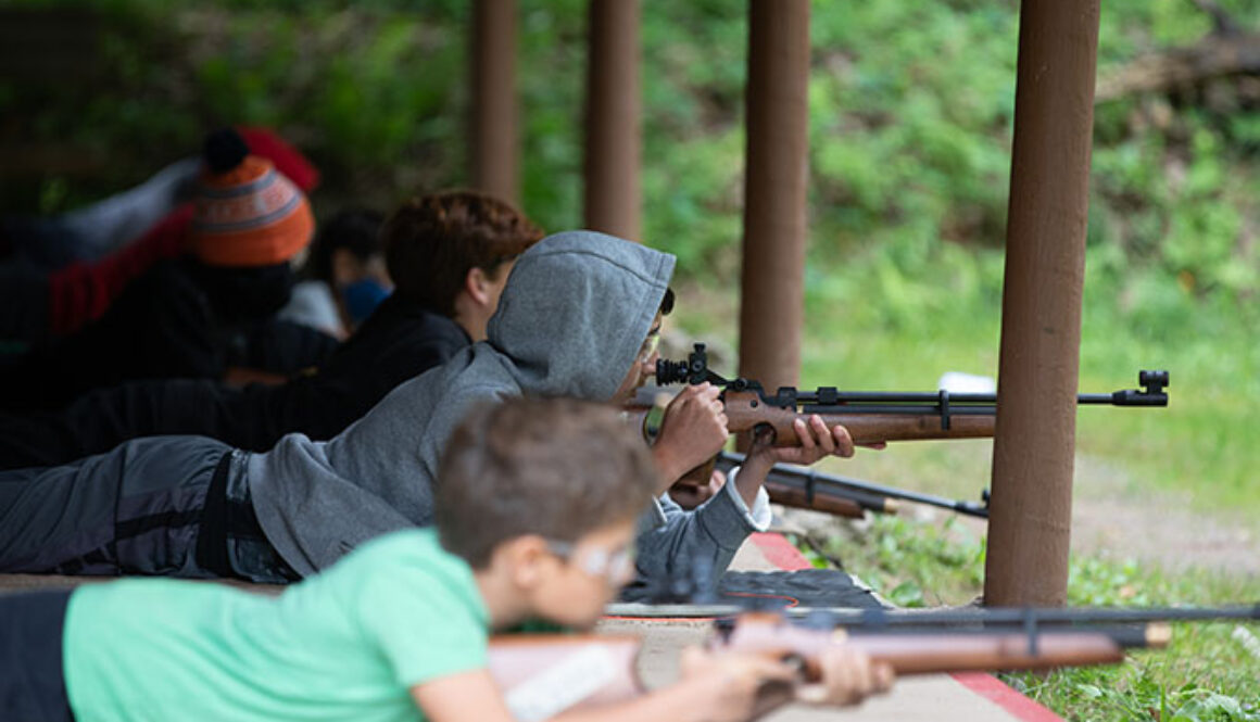 A group of boys at North Star Camp for Boys participate in a riflery training activity by laying on the ground and aiming.