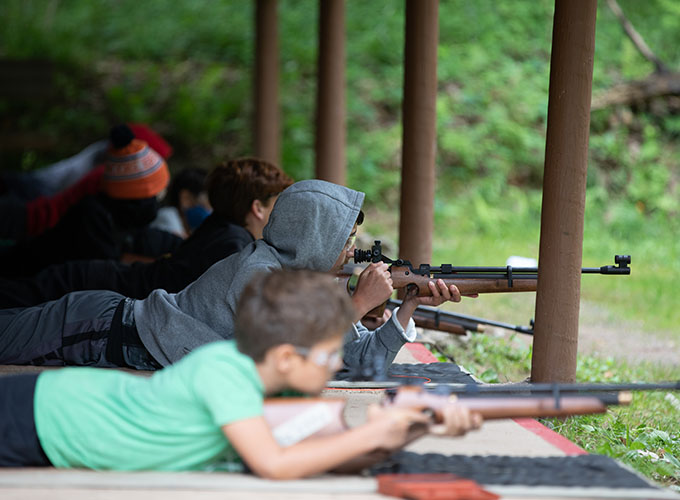 A group of boys at North Star Camp for Boys participate in a riflery training activity by laying on the ground and aiming.