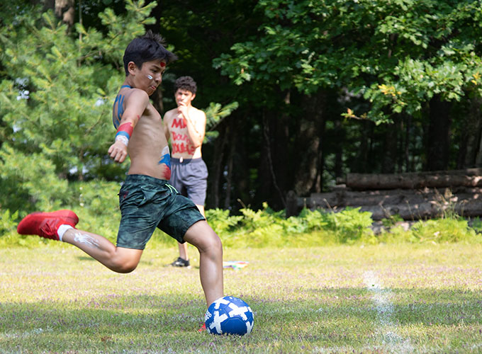 A camper wearing body paint kicks a soccer ball at North Star Camp for Boys.