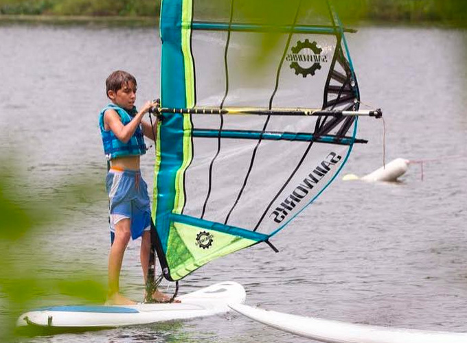 A young boy at summer camp stands on a windsurf in a Wisconsin lake.