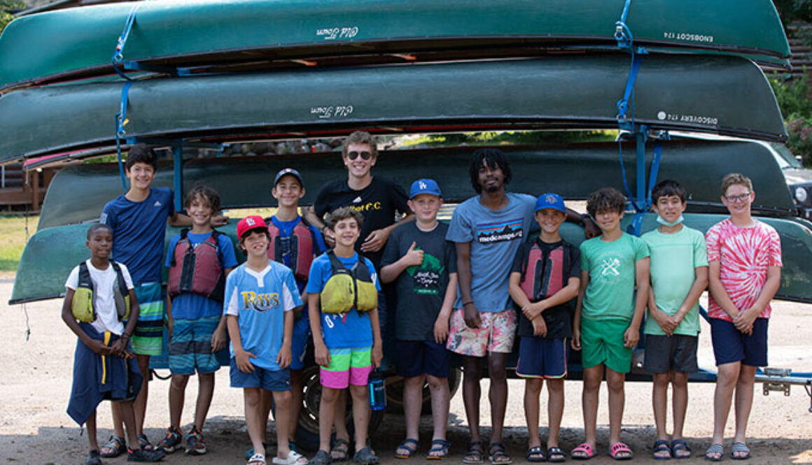 A group of campers and counselors stand in front of a stack of canoes at North Star Camp for Boys.