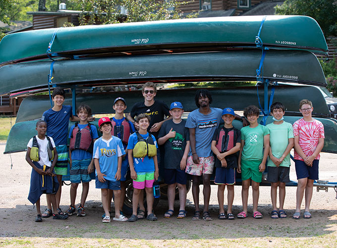 A group of campers and counselors stand in front of a stack of canoes at North Star Camp for Boys.