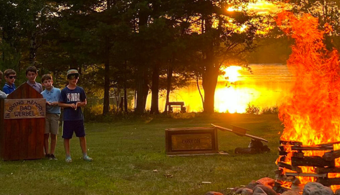 A group of campers watch a bonfire burn as the sun sets over Spider Lake in Hayward, WI at North Star Camp for Boys.