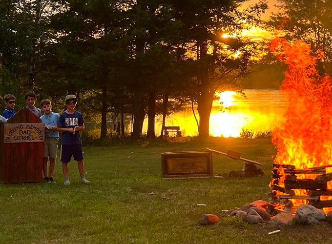 A group of campers watch a bonfire burn as the sun sets over Spider Lake in Hayward, WI at North Star Camp for Boys.