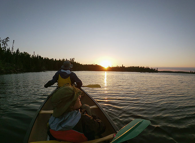 A camper sitting in the back of a tandem canoe admires the sunset on the lake at North Star Camp for Boys.