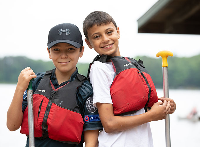 Two elementary-aged North Star Camp for Boys campers wearing life jackets pose with their canoe ores.