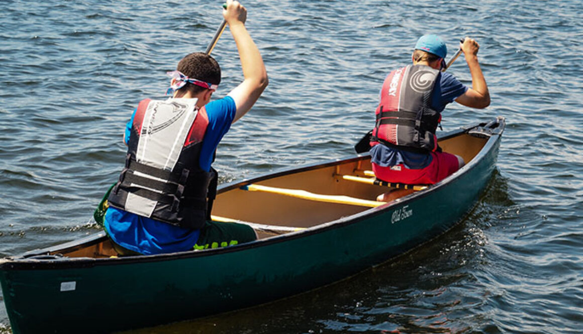 Two campers wearing life jackets paddle on the left side of their tandem canoe at North Star Camp for Boys.