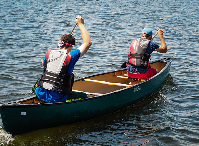 Two campers wearing life jackets paddle on the left side of their tandem canoe at North Star Camp for Boys.