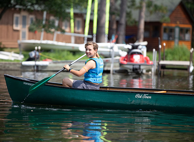 A camper at North Star Camp for Boys smiles while paddling in a canoe.