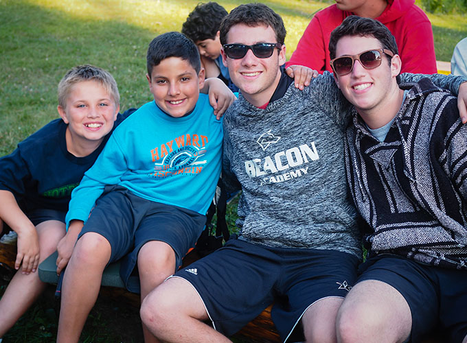 Two elementary-aged campers smile with two camp counselors at North Star Camp for Boys.