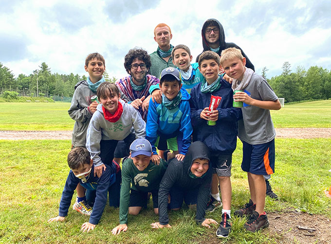 A group of campers smile while posing in a human pyramid. Four other campers and three counselors stand behind them at North Star Camp for Boys.