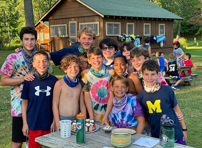 A group of campers and junior counselors smile around a picnic table that has a birthday cake on it at North Star Camp for Boys.