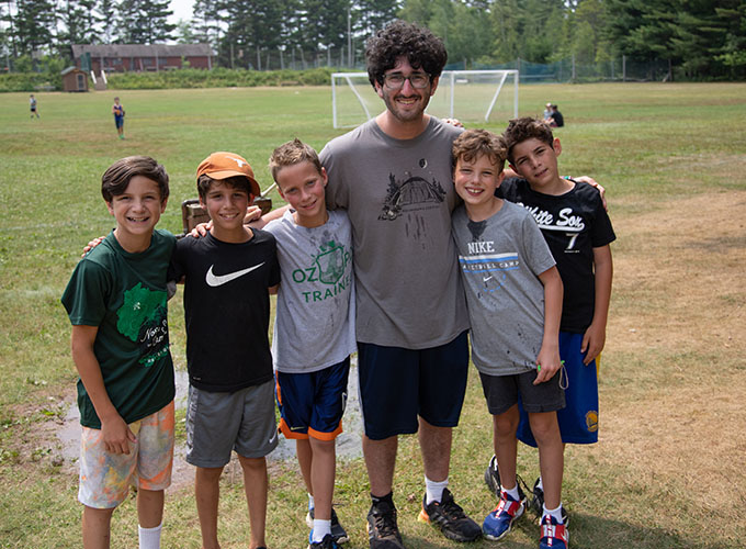 Five campers smile with a staff member while standing on the soccer field at North Star Camp for Boys.