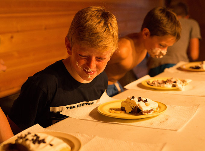 Two boys with frosting all over their faces eat a piece of pie while participating in a no-hands eating competition at North Star Camp for Boys.