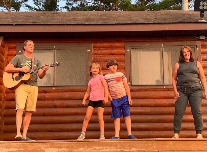 A man plays guitar while a woman, girl, and boy perform on stage alongside him at North Star Camp for Boys.