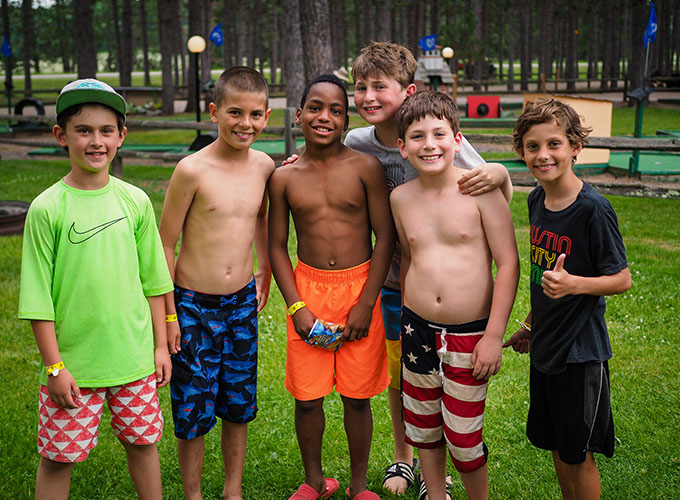 A group of elementary-aged boys wearing swim trunks smile at North Star Camp for Boys.