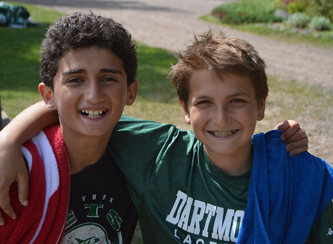 Two campers smile with their arms around each others, they both have towels thrown on their shoulders at North Star Camp for Boys.