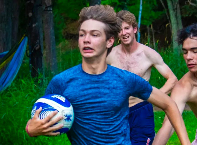 Two campers and a staff member run while playing a game of speedball, one camper is trying to steal the ball from another at North Star Camp for Boys.