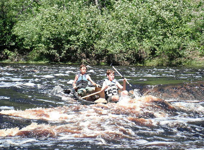 Two campers from North Star Camp for Boys sit in a tandem canoe, while navigating rapid waters during a wilderness trip.