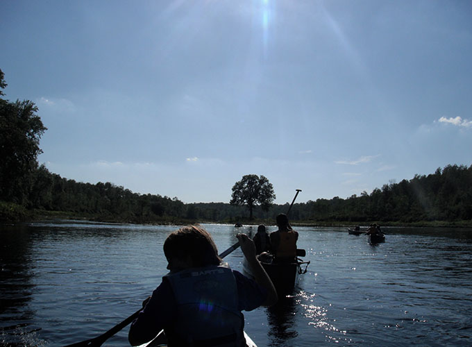 North Star Camp for Boys campers row through a river during daytime in canoes.