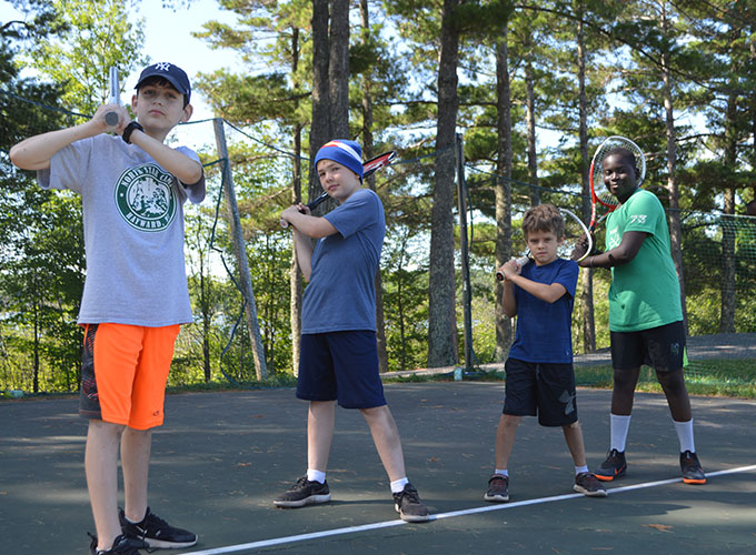 Four campers pose with their tennis racquets on a tennis court at North Star Camp for Boys.