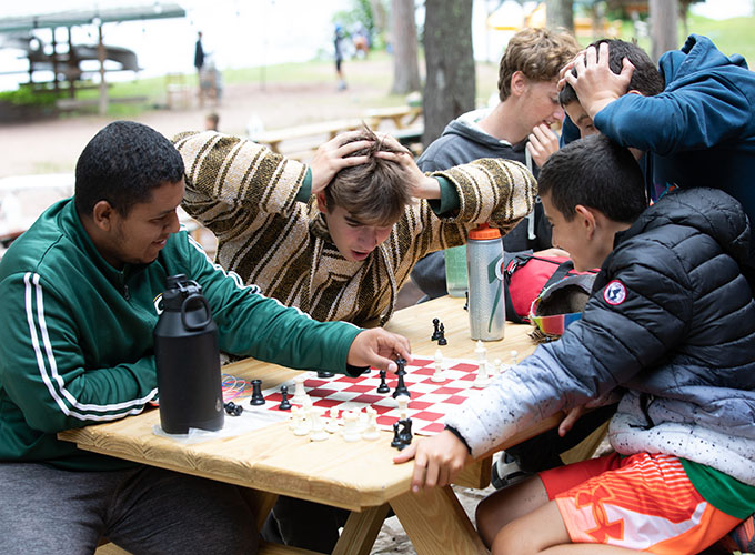 Two campers with their hands on their heads in shock watch as their smiling teammates make a move in a game of chess at North Star Camp for Boys.