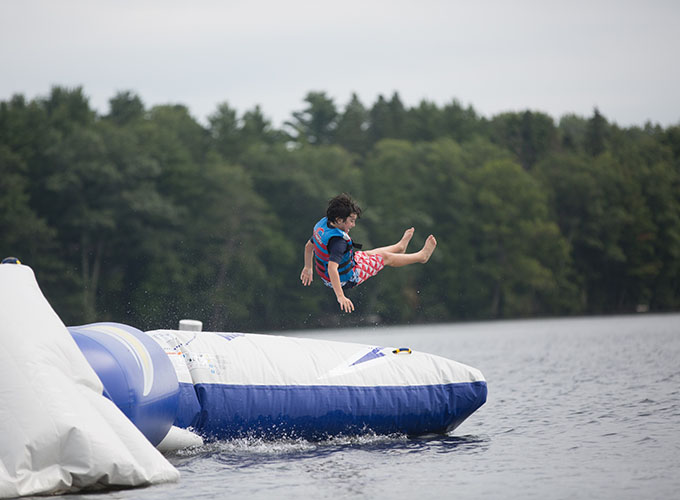 A camper flies in the air after bouncing on the water trampoline in Spider Lake at North Star Camp for Boys.